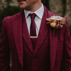 a man wearing a red suit and tie with a flower in his lapel pocket