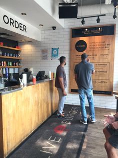 two men are standing at the counter in a coffee shop, one is ordering something