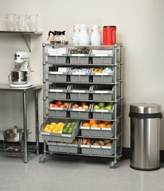 a metal shelving unit with bins filled with fruits and vegetables next to a trash can