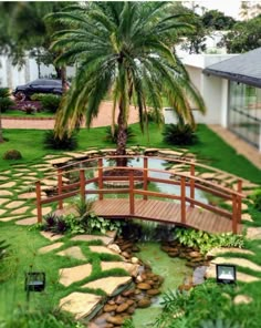 a wooden bridge over a small pond surrounded by green grass and palm trees in front of a house