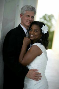 a man and woman are posing for a wedding photo in front of a wall with columns