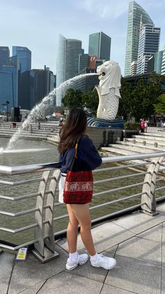 a woman standing next to a metal railing near a body of water with buildings in the background