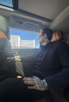 a man sitting in the back seat of a car with tattoos on his arm and hand