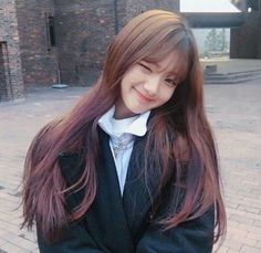 a young woman with long hair standing on a brick walkway wearing a black jacket and white shirt