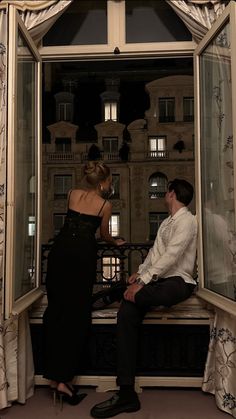 a man and woman sitting on a window sill in front of a large building