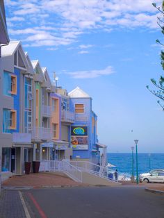 a row of multi - colored buildings next to the ocean with cars parked on the street