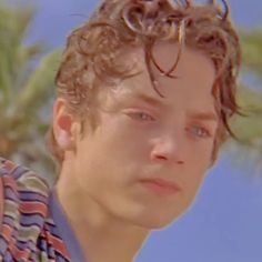 a young man with curly hair and glasses on his head looking at the camera while standing in front of palm trees