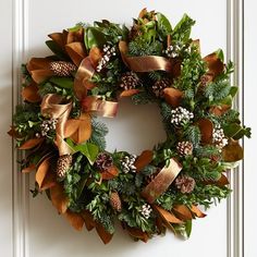 a christmas wreath with pine cones and evergreens on the front door, decorated with gold ribbon