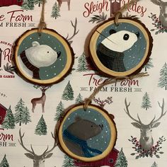 three christmas ornaments hanging from strings with deer and snowman designs on them, all decorated in wood slices