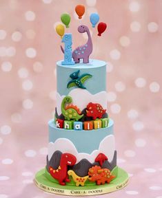 a three tiered cake decorated with dinosaurs and balloons for a baby's first birthday