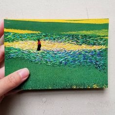 a hand holding up a piece of paper with an image of a person standing in the grass