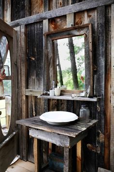 a rustic bathroom with wooden walls and wood flooring is pictured in this image, there is a mirror on the wall