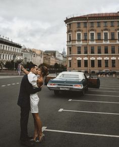 a man and woman kissing in the middle of a parking lot next to a car