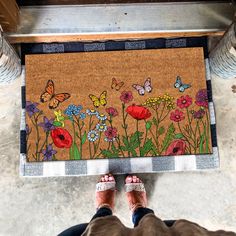 a person standing in front of a door mat with flowers and butterflies on it