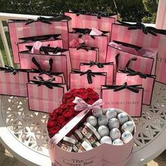 pink and black boxes filled with chocolates on top of a white tablecloth next to red roses