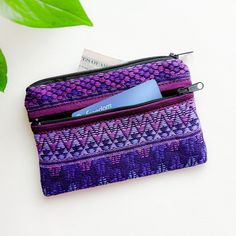 a purple and blue wallet sitting on top of a table next to a green leaf