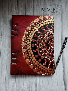 a red and black notebook with an intricate design on the cover, sitting on a wooden surface