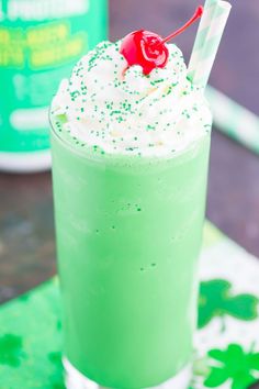 a green drink with whipped cream and a cherry garnish on the top is sitting on a table