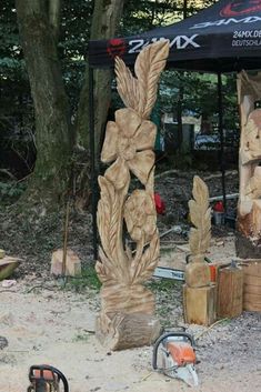 a large wooden sculpture sitting on top of a sandy ground next to a forest filled with trees