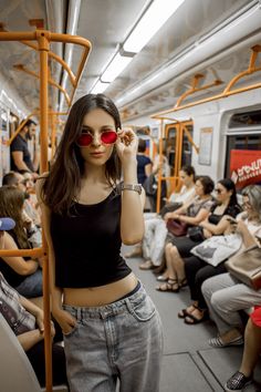 a woman wearing red sunglasses standing on a subway car with people sitting in the background