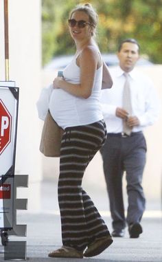 a pregnant woman walking down the street with a stop sign in front of her and a man behind her