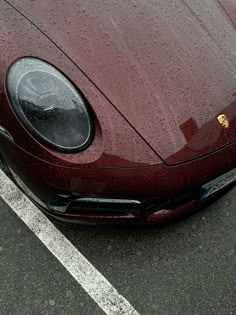 a red sports car parked in a parking lot with rain drops on the hood and headlight