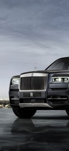 the front end of a black rolls royce parked in a parking lot with city lights behind it