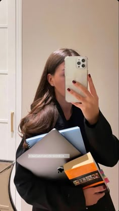 a woman taking a selfie with her cell phone in front of her face while holding several folders