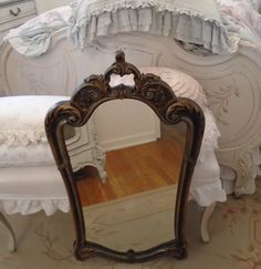 there is a mirror on the floor in front of a white chair and bed with ruffled bedspread