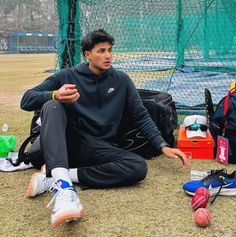 a man sitting on the ground next to some sports equipment and backpacks in front of him