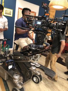 three men standing in front of a camera set up on a dolly with two other men looking at the camera