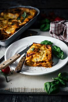 a white plate topped with lasagna next to a pan of lasagna