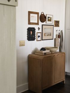 a wooden cabinet with pictures on the wall above it and other items hanging on the wall