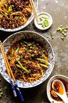 two bowls filled with noodles and vegetables next to chopsticks on a table top