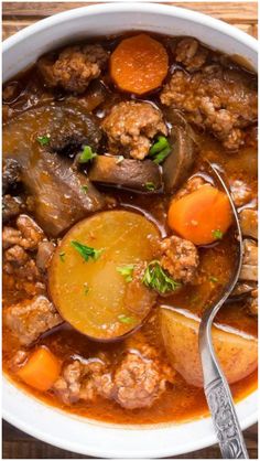 a white bowl filled with meat and vegetables next to a spoon on top of a wooden table