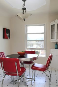 a dining room table with four red chairs and a bowl of fruit on the table