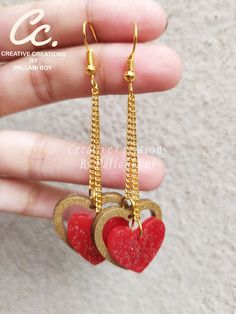 two heart shaped earrings with chains hanging from them on a hand held by someone's finger