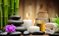 spa items with candles, towels and flowers on wooden table in front of bamboo background