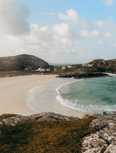 a sandy beach next to the ocean under a cloudy blue sky