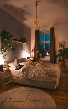 a bed room with a neatly made bed next to a window and potted plants