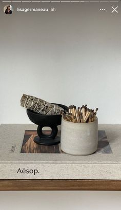 a white cup with matches in it sitting on top of a wooden table next to a book