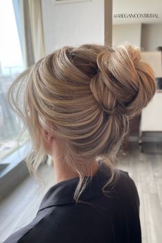 a woman with blonde hair styled into a low bun in a living room, looking out the window