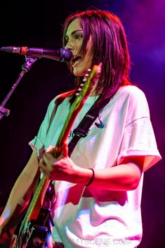 a woman singing into a microphone while holding a guitar in front of her face on stage