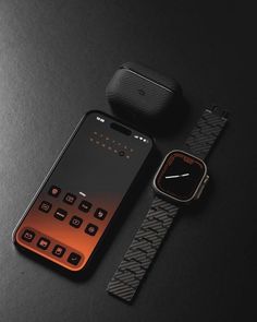 an orange and black cell phone next to a smart watch on a black surface with a matching strap