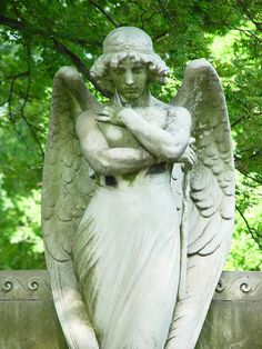 an angel statue holding a pipe in its hands and standing on a stone wall with trees behind it