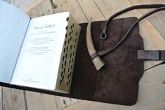 an open book on top of a table next to a leather bag with a wooden handle