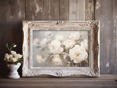 a white vase filled with flowers sitting next to a painting on top of a wooden table