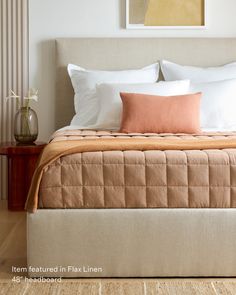 a bed with pillows and blankets on top of it next to a night stand in front of a painting