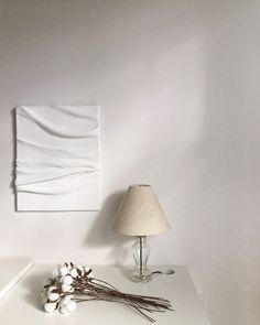 a white table with a lamp and some cotton on it in front of a painting