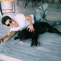 a man laying on the floor next to a black dog with sunglasses on his face